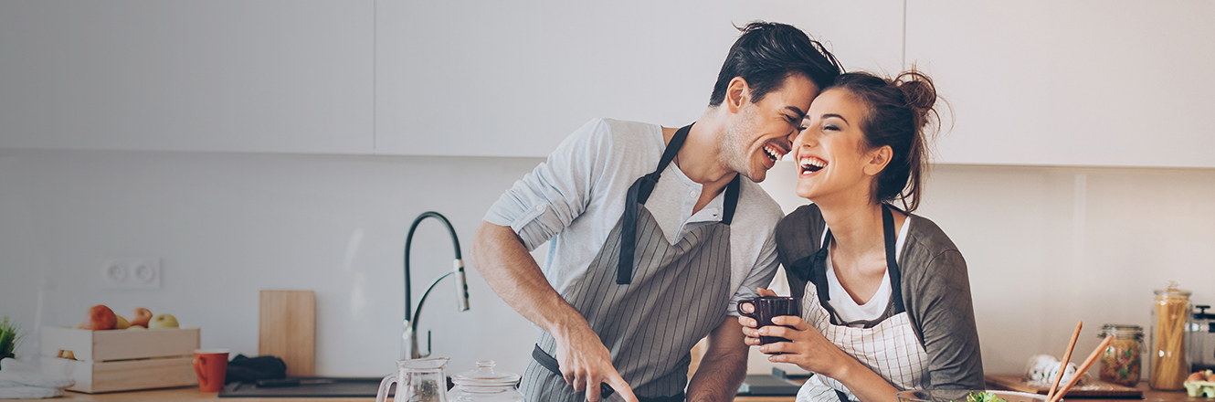 young couple laughing while cooking together in kitchen