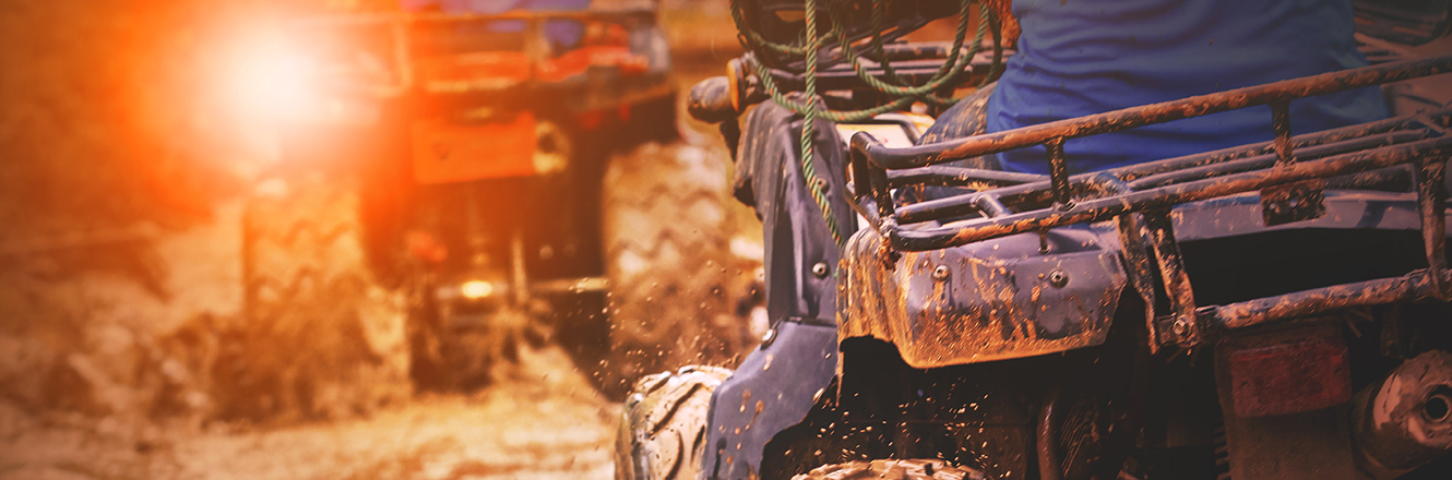 Two ATV's driving through a muddy trail 