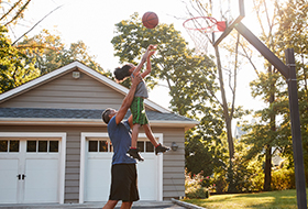 father and son playing basketball in yard