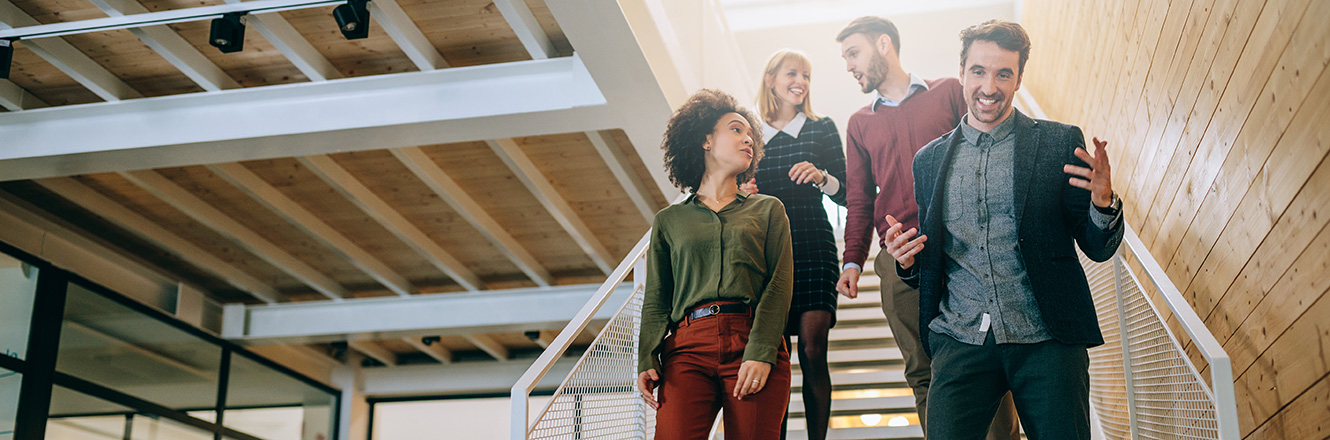 Four business colleagues in animated conversation, walking through a bright open office stairway