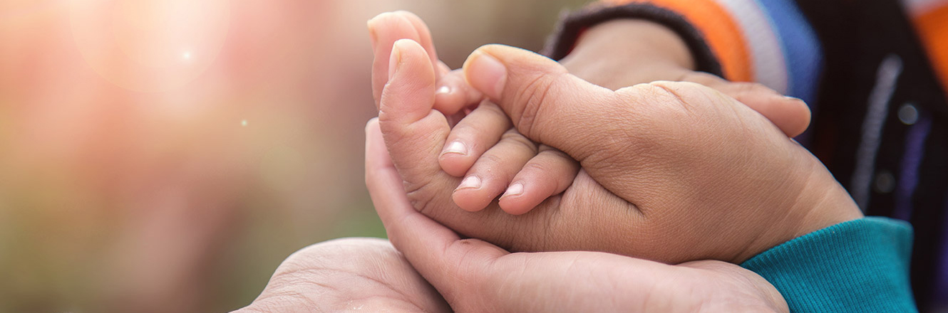 Close up of parents holding the hand of a small child 