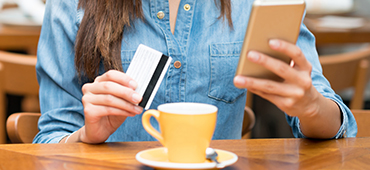 woman using phone and card in cafe with tea cup