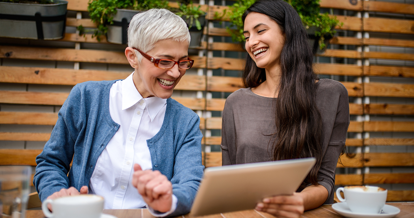 two women at cafe looking at a tablet talking and smiling