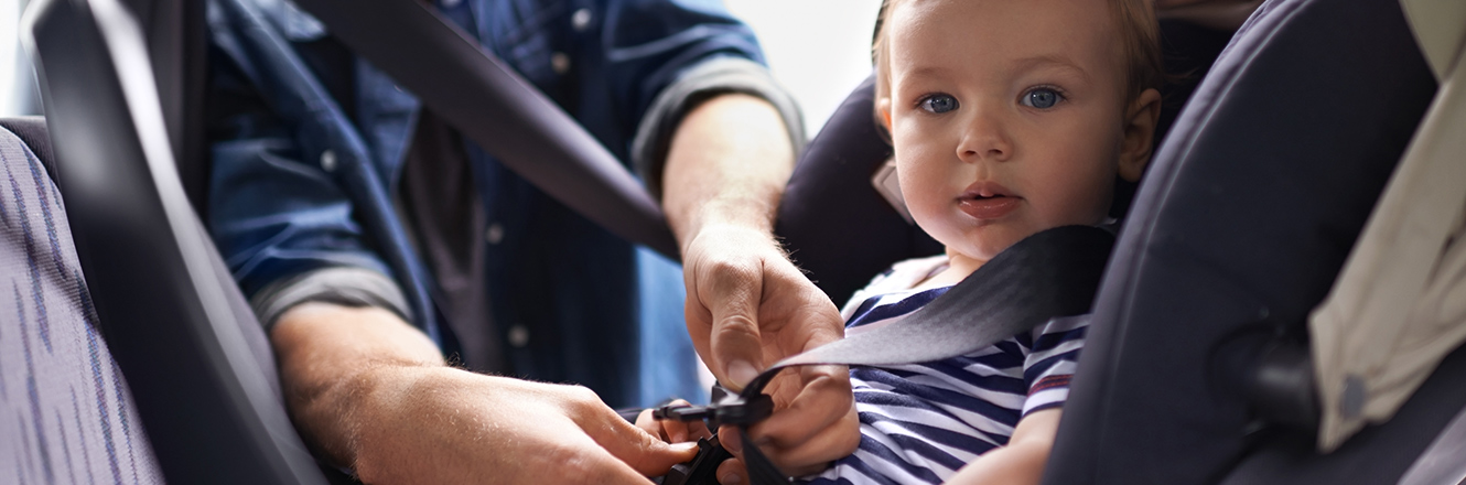 father buckling infant into car seat