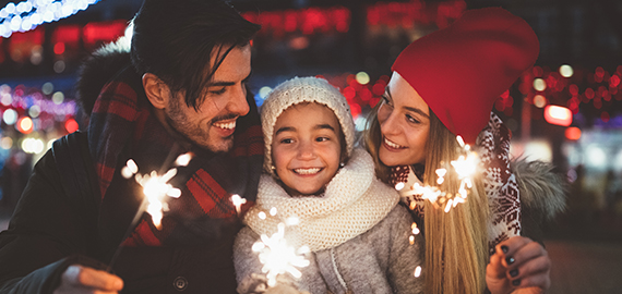 parents and daughter wearing winter clothes holding sparklers outside