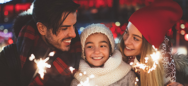 parents and daughter wearing winter clothes holding sparklers outside