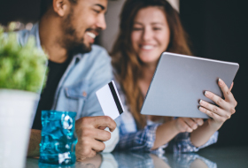 A young couple smiling holding a tablet and a debit/credit card