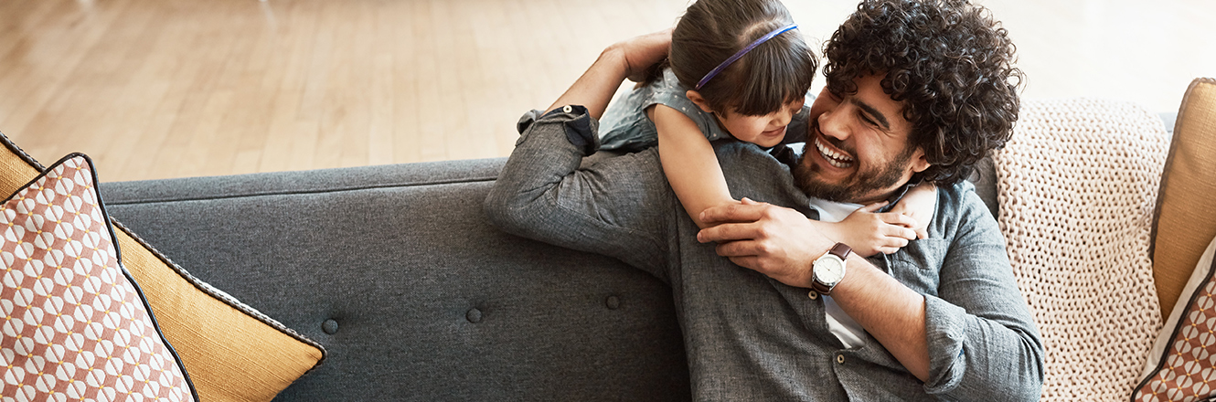 young daughter hugging fathers neck while sitting on a couch