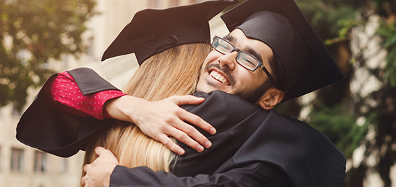 two high school graduates hugging after graduation