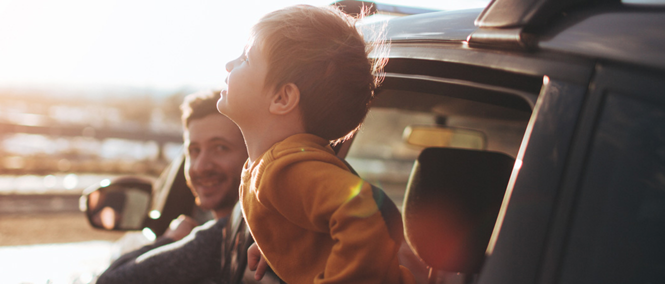 Young child leaning out the window of a parked car, looking at the beach. 