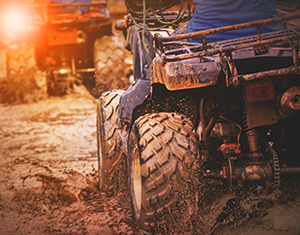 Two ATV's driving through a muddy trail 