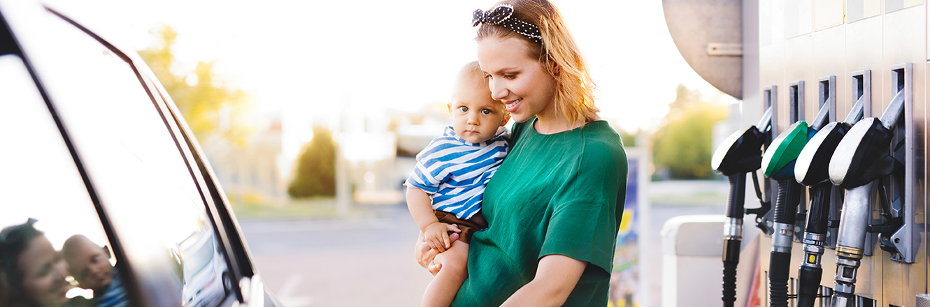 mother filling car with gas while holding baby