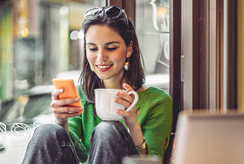 woman looking at phone while drinking coffee