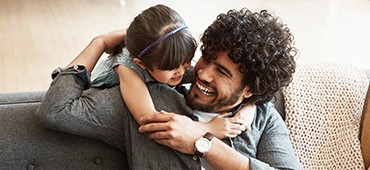 young daughter hugging fathers neck while sitting on a couch