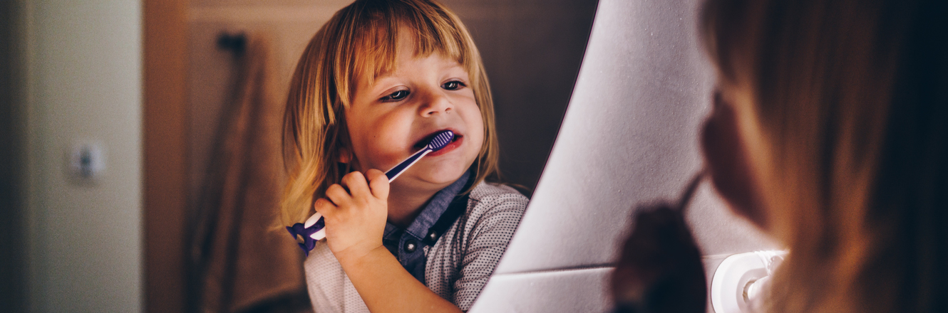 small child concentrating on brushing teeth in the mirror