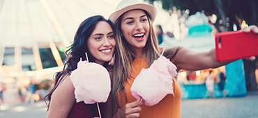 two young women taking selfie at carnival with cotton candy