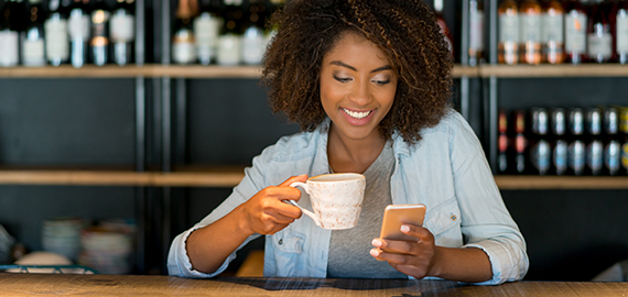 woman looking at phone holding coffee cup at table