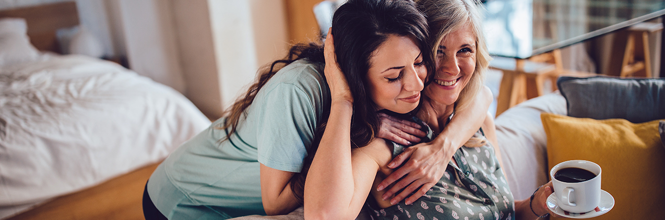 Adult daughter hugging mother on couch