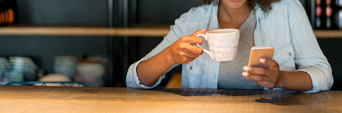 woman looking at phone holding coffee cup at table