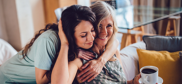 Adult daughter hugging mother on couch