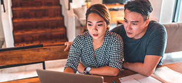 couple sitting at kitchen table looking at computer