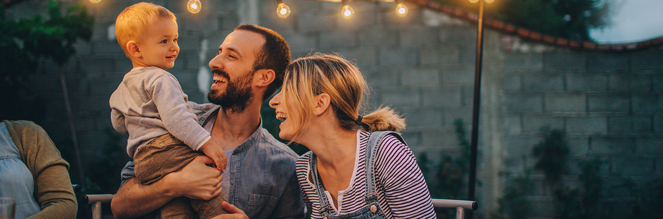 two young parents smiling at their son outdoors at a dinner table with friends