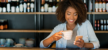 woman looking at phone holding coffee cup at table