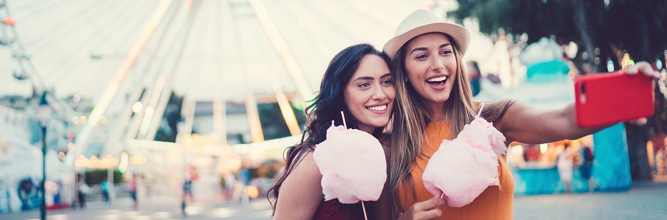 two young women taking selfie at carnival with cotton candy