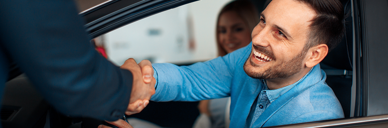 Man leaning out car window to shake hands with salesperson