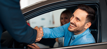 Man leaning out car window to shake hands with salesperson